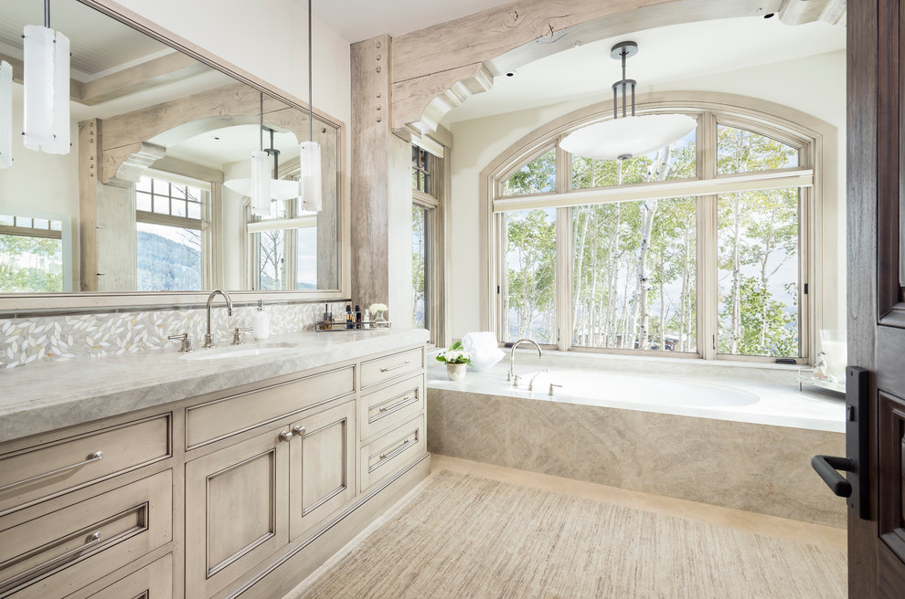 Inspiration for an expansive country bathroom in Salt Lake City with beige cabinets, marble benchtops, recessed-panel cabinets, an undermount tub, gray tile, mosaic tile, white walls, an undermount sink, beige floor and grey benchtops.