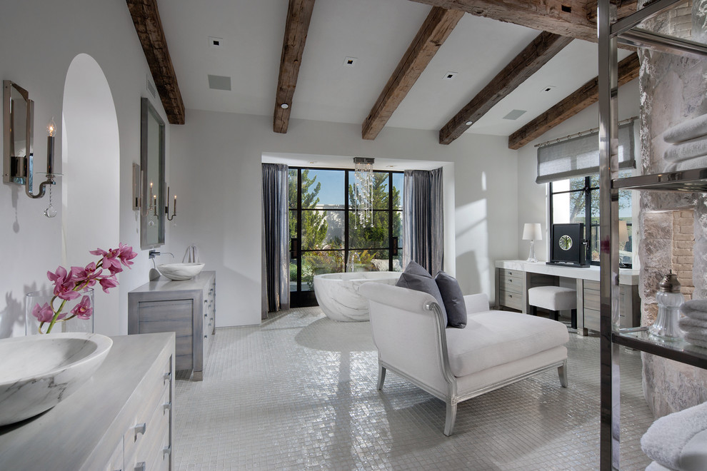 Photo of an expansive mediterranean master bathroom in Orange County with furniture-like cabinets, medium wood cabinets, a freestanding tub, an open shower, a one-piece toilet, white tile, glass tile, white walls, marble floors, a drop-in sink and wood benchtops.