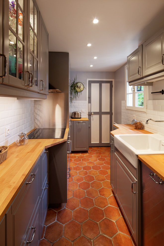 Inspiration for a small contemporary galley separate kitchen in Paris with a farmhouse sink, flat-panel cabinets, grey cabinets, wood benchtops, white splashback, subway tile splashback, panelled appliances, terra-cotta floors and no island.