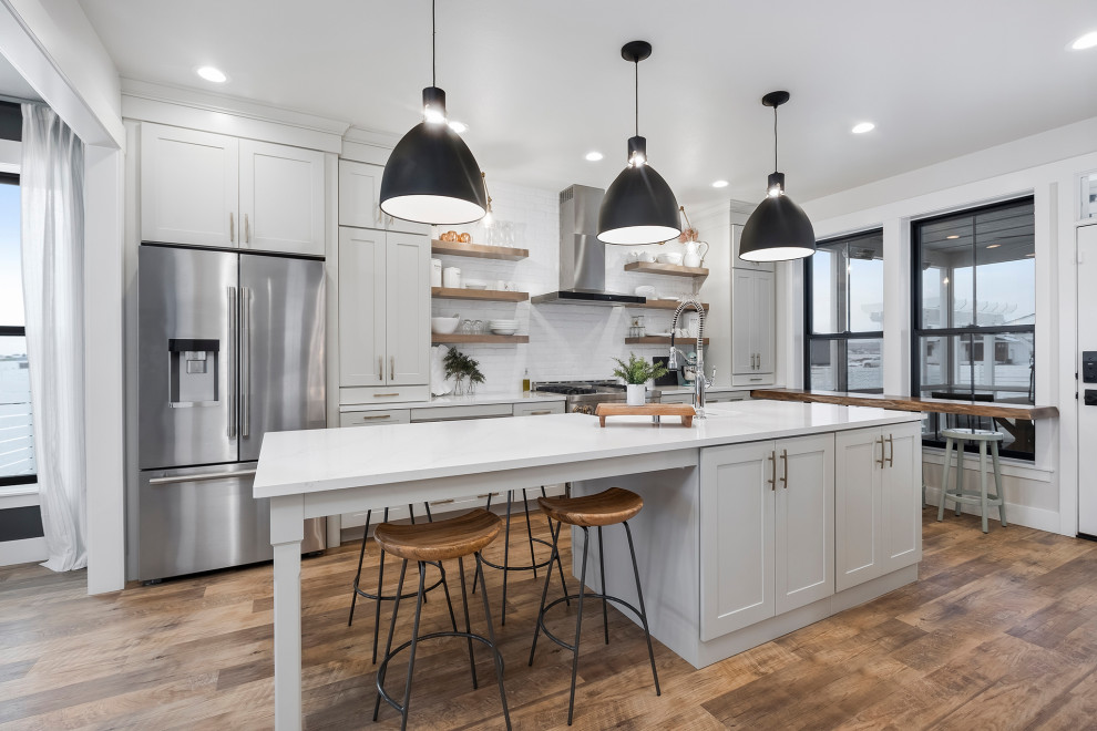 This is an example of a transitional kitchen in Other with shaker cabinets, grey cabinets, white splashback, stainless steel appliances, with island, brown floor and white benchtop.