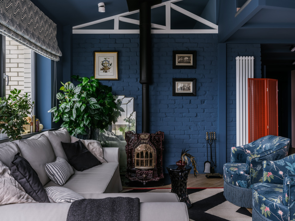Large bohemian mezzanine living room feature wall in Moscow with a reading nook, blue walls, medium hardwood flooring, a wood burning stove, a metal fireplace surround, no tv, brown floors, a vaulted ceiling and brick walls.