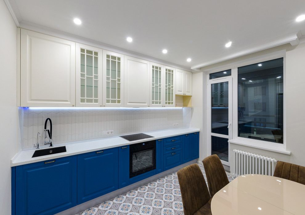 Пример оригинального дизайна: прямая кухня среднего размера в современном стиле с обеденным столом, врезной мойкой, фасадами с утопленной филенкой, синими фасадами, столешницей из акрилового камня, белым фартуком, фартуком из керамической плитки, черной техникой, полом из керамической плитки, разноцветным полом, белой столешницей, многоуровневым потолком и двухцветным гарнитуром без острова
