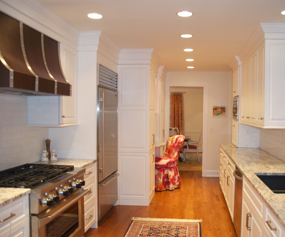 This is an example of a mid-sized traditional galley separate kitchen in Cincinnati with an undermount sink, raised-panel cabinets, white cabinets, granite benchtops, white splashback, subway tile splashback, stainless steel appliances, medium hardwood floors and no island.