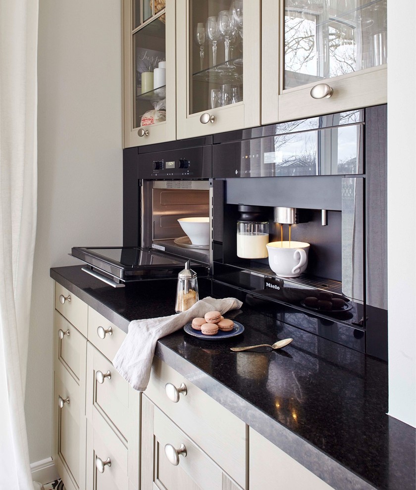 Inspiration for an expansive traditional galley separate kitchen in Berlin with an undermount sink, raised-panel cabinets, green cabinets, granite benchtops, black splashback, stone tile splashback, black appliances, porcelain floors and with island.
