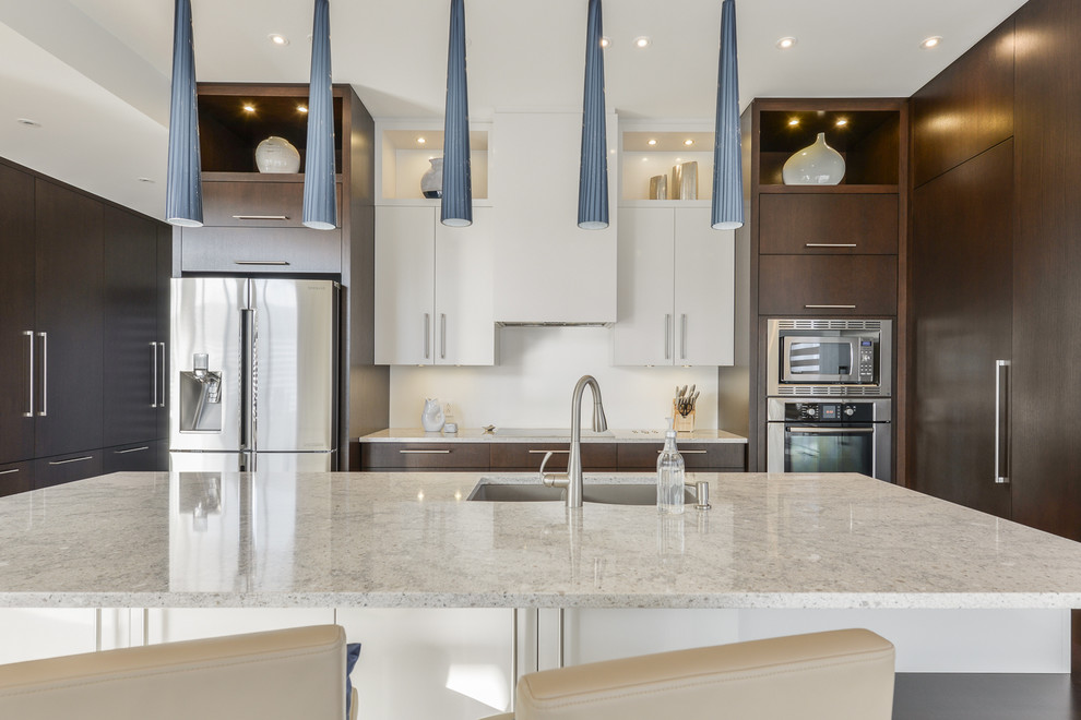 Expansive contemporary single-wall open plan kitchen in Montreal with an undermount sink, flat-panel cabinets, dark wood cabinets, white splashback, ceramic splashback, stainless steel appliances, porcelain floors, with island and quartzite benchtops.