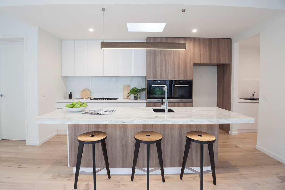 Photo of an expansive contemporary galley eat-in kitchen in Melbourne with an undermount sink, flat-panel cabinets, medium wood cabinets, marble benchtops, white splashback, glass sheet splashback, black appliances, laminate floors, with island and brown floor.