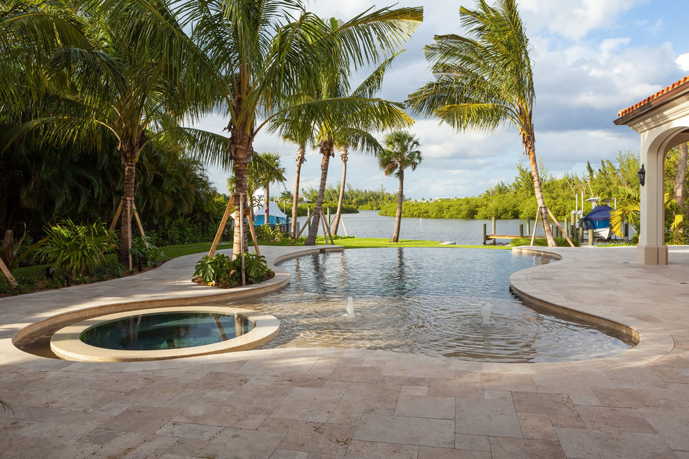 Photo of a large tropical backyard custom-shaped infinity pool in Miami with a hot tub and tile.