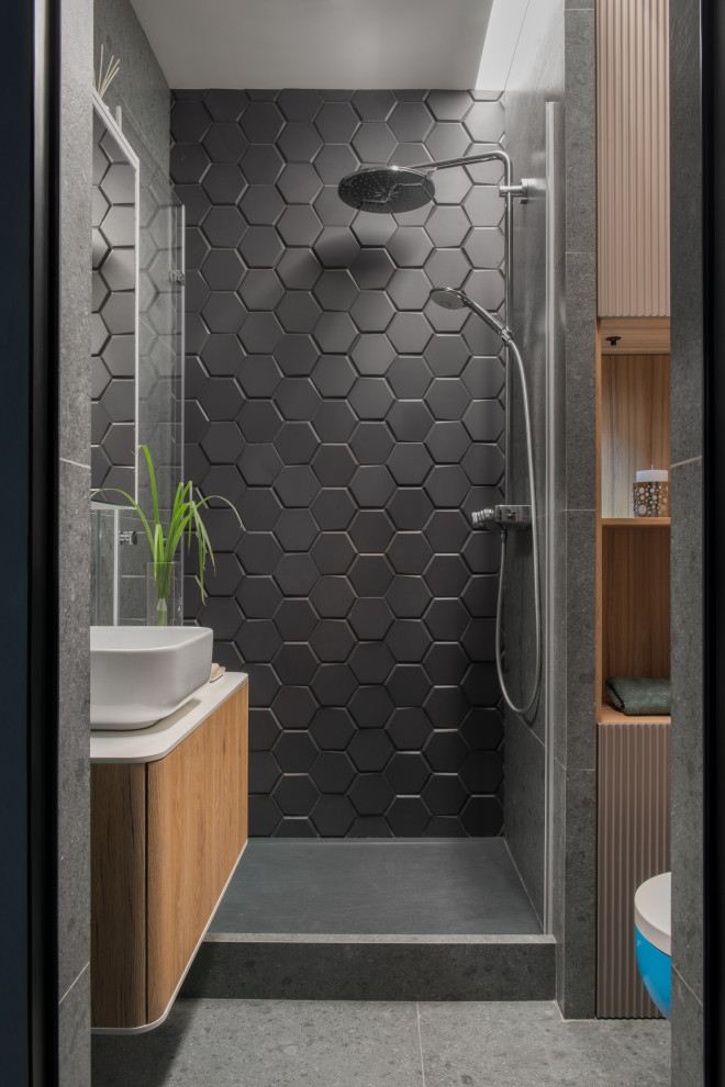 Пример оригинального дизайна: ванная комната среднего размера в современном стиле с плоскими фасадами, светлыми деревянными фасадами, инсталляцией, черной плиткой, керамической плиткой, серыми стенами, полом из керамогранита, накладной раковиной, столешницей из искусственного камня, серым полом, белой столешницей, акцентной стеной и подвесной тумбой