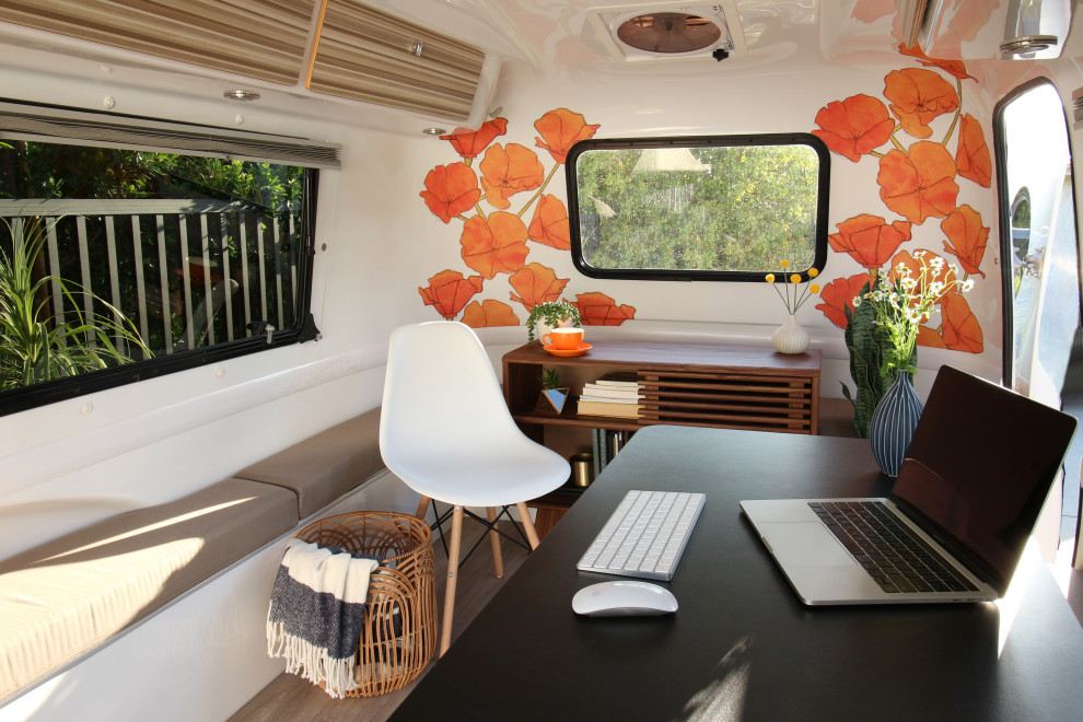 Immagine di un piccolo studio minimalista con pareti arancioni, pavimento in laminato, scrivania autoportante, pavimento grigio e carta da parati