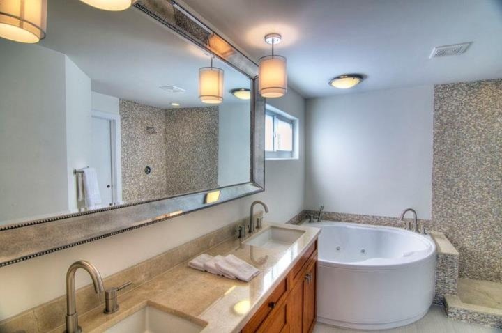 Inspiration for a mid-sized traditional master bathroom in Miami with shaker cabinets, light wood cabinets, a corner tub, an open shower, a one-piece toilet, beige tile, brown tile, white tile, pebble tile, white walls, vinyl floors, an undermount sink and granite benchtops.