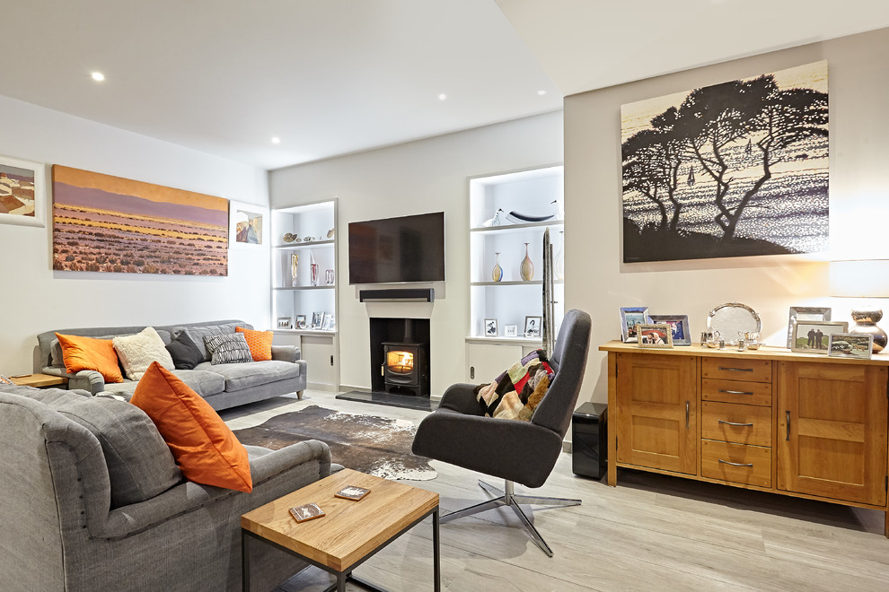 Transitional living room in Surrey with white walls, a wood stove, a wall-mounted tv and grey floor.