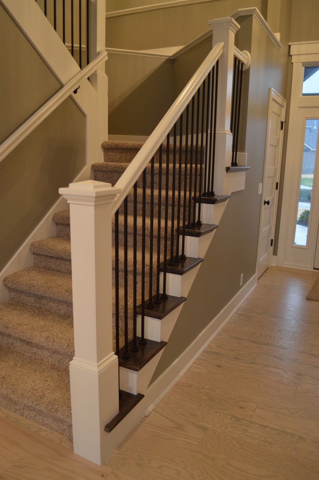 Photo of a large arts and crafts carpeted u-shaped staircase in Other with carpet risers and metal railing.