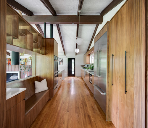 Modern wood finish galley kitchen cabinets with built-in seating, stainless steel appliances, and a sleek corridor layout featuring natural light and warm flooring