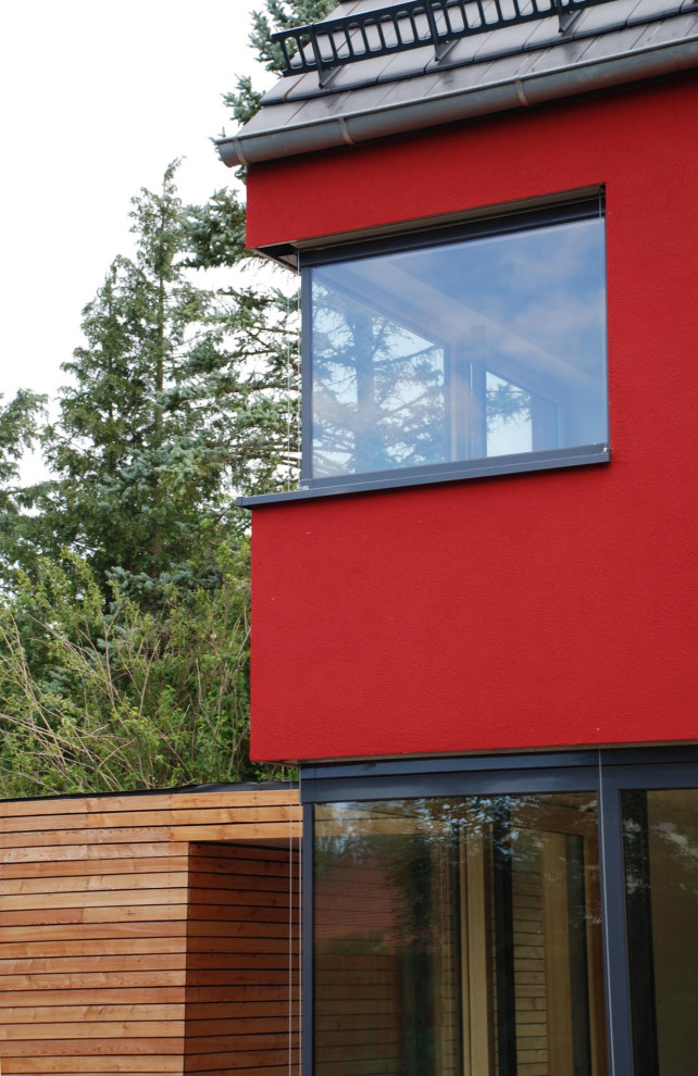 Modernes Einfamilienhaus mit Putzfassade, roter Fassadenfarbe, Satteldach, Ziegeldach und grauem Dach in München