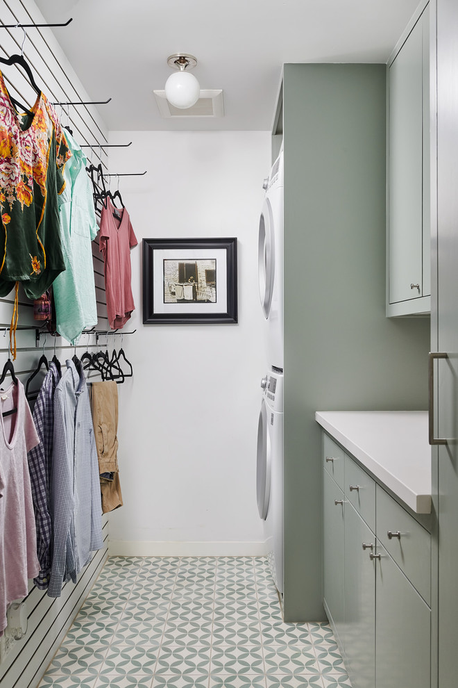 Photo of a mid-sized contemporary galley dedicated laundry room in Houston with flat-panel cabinets, green cabinets, quartz benchtops, white walls, ceramic floors, a stacked washer and dryer, green floor and white benchtop.