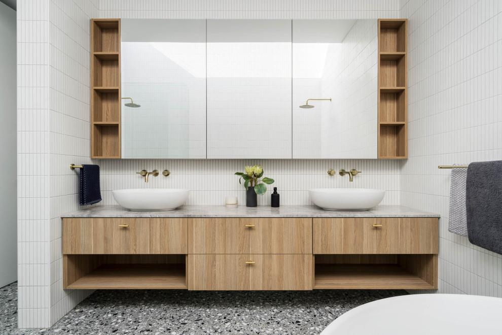 This is an example of a large contemporary master bathroom in Melbourne with light wood cabinets, a freestanding tub, gray tile, mosaic tile, white walls, porcelain floors, a vessel sink, grey floor, grey benchtops, an enclosed toilet, a double vanity and a floating vanity.