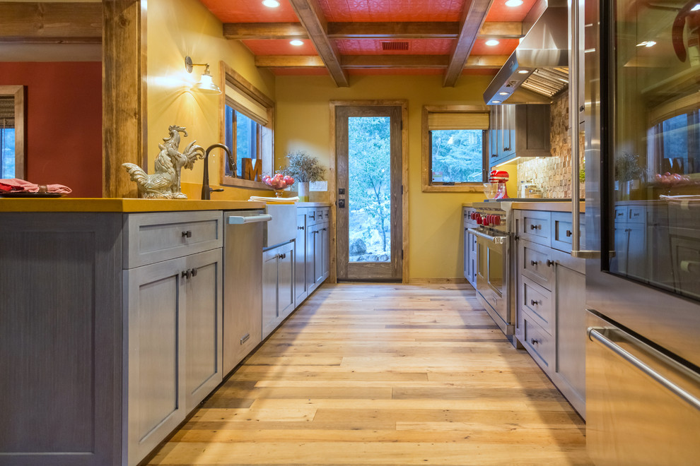 Design ideas for a mid-sized country galley open plan kitchen in Los Angeles with a farmhouse sink, shaker cabinets, grey cabinets, limestone benchtops, multi-coloured splashback, mosaic tile splashback, stainless steel appliances and light hardwood floors.