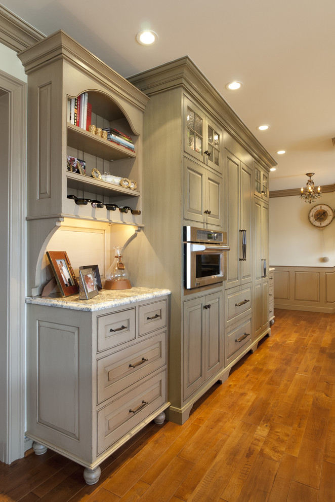 This is an example of a mid-sized traditional u-shaped eat-in kitchen in Philadelphia with a farmhouse sink, raised-panel cabinets, grey cabinets, granite benchtops, white splashback, subway tile splashback, stainless steel appliances, medium hardwood floors and a peninsula.