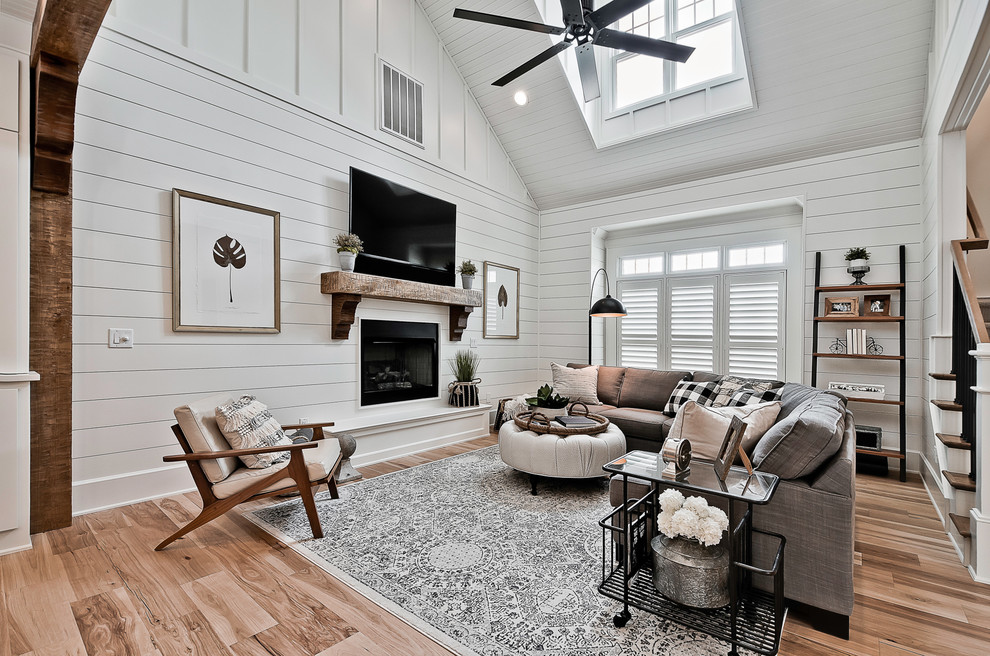 Inspiration for a large country open concept family room in Other with white walls, a standard fireplace, a wood fireplace surround, a wall-mounted tv, medium hardwood floors and brown floor.