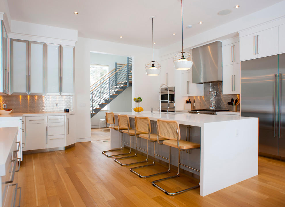 Photo of a contemporary kitchen in New York with an undermount sink, flat-panel cabinets, white cabinets, metallic splashback, metal splashback, stainless steel appliances, medium hardwood floors and with island.