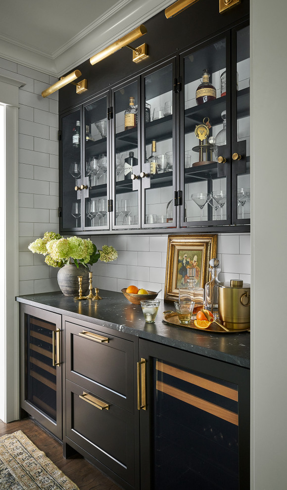 Design ideas for a mid-sized transitional kitchen pantry in Chicago with a farmhouse sink, shaker cabinets, quartzite benchtops, white splashback, subway tile splashback, panelled appliances, medium hardwood floors, with island, black benchtop and black cabinets.