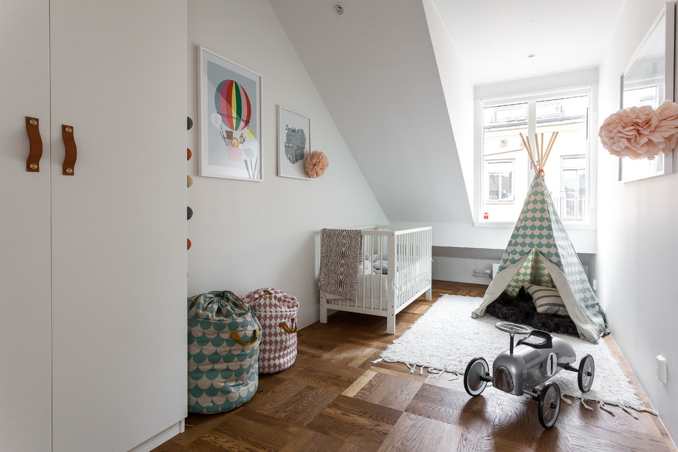 Photo of a mid-sized scandinavian gender-neutral nursery in Stockholm with white walls, light hardwood floors and brown floor.