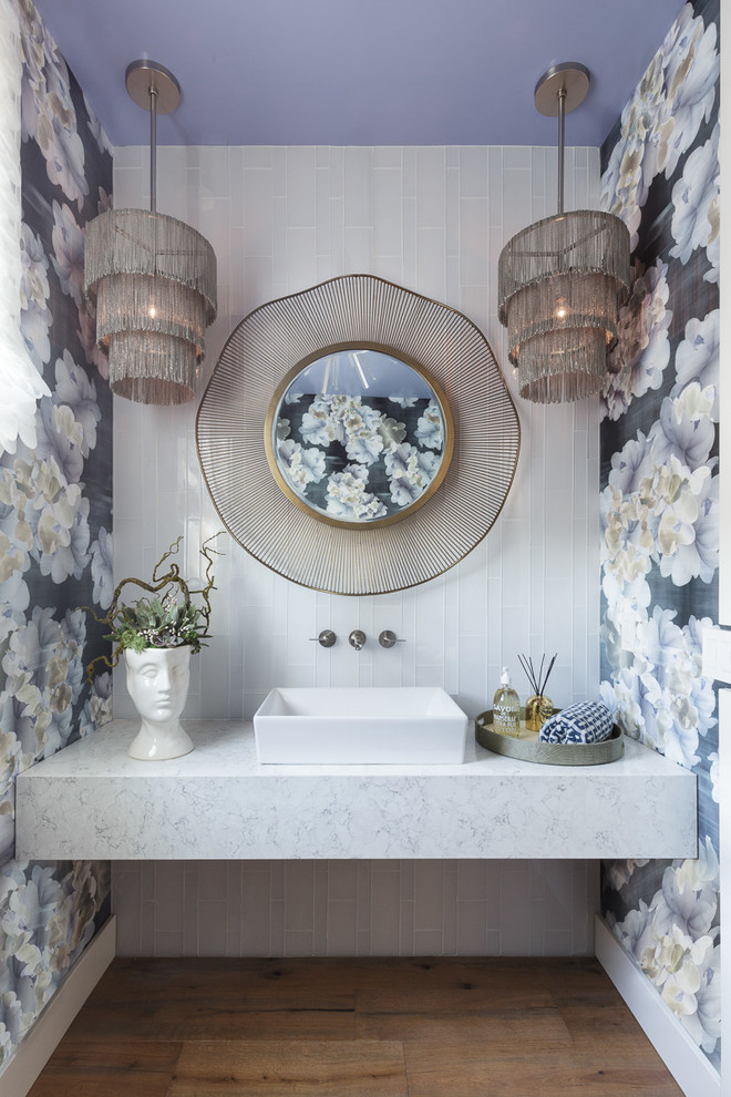 Photo of a mid-sized transitional powder room in San Francisco with a vessel sink, furniture-like cabinets, white cabinets, a one-piece toilet, engineered quartz benchtops, brown floor, white tile, blue walls and medium hardwood floors.
