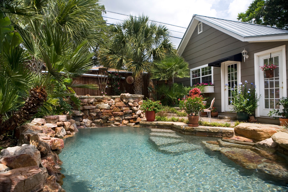 Small country backyard custom-shaped natural pool in Austin with natural stone pavers and a hot tub.
