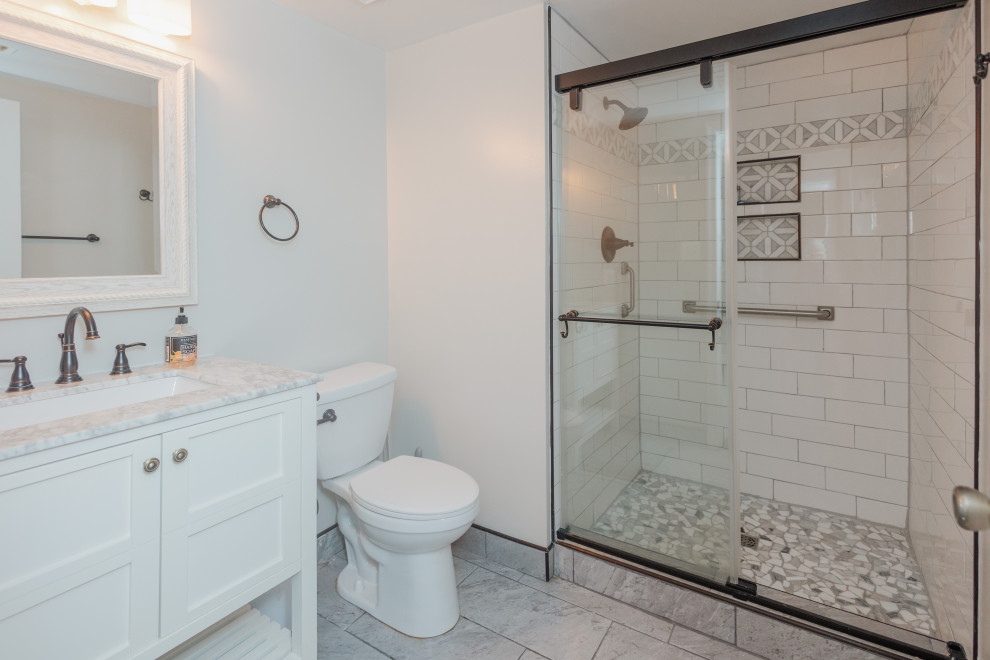 Inspiration for a medium sized traditional shower room bathroom in DC Metro with recessed-panel cabinets, white cabinets, an alcove shower, a two-piece toilet, white tiles, ceramic tiles, white walls, ceramic flooring, an integrated sink, marble worktops, grey floors, a sliding door, white worktops, a single sink and a freestanding vanity unit.