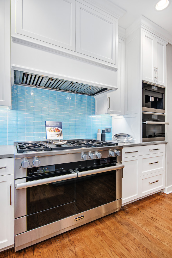 Inspiration for a large transitional l-shaped medium tone wood floor and brown floor kitchen remodel in Chicago with a farmhouse sink, shaker cabinets, white cabinets, quartzite countertops, blue backsplash, glass tile backsplash, stainless steel appliances and an island