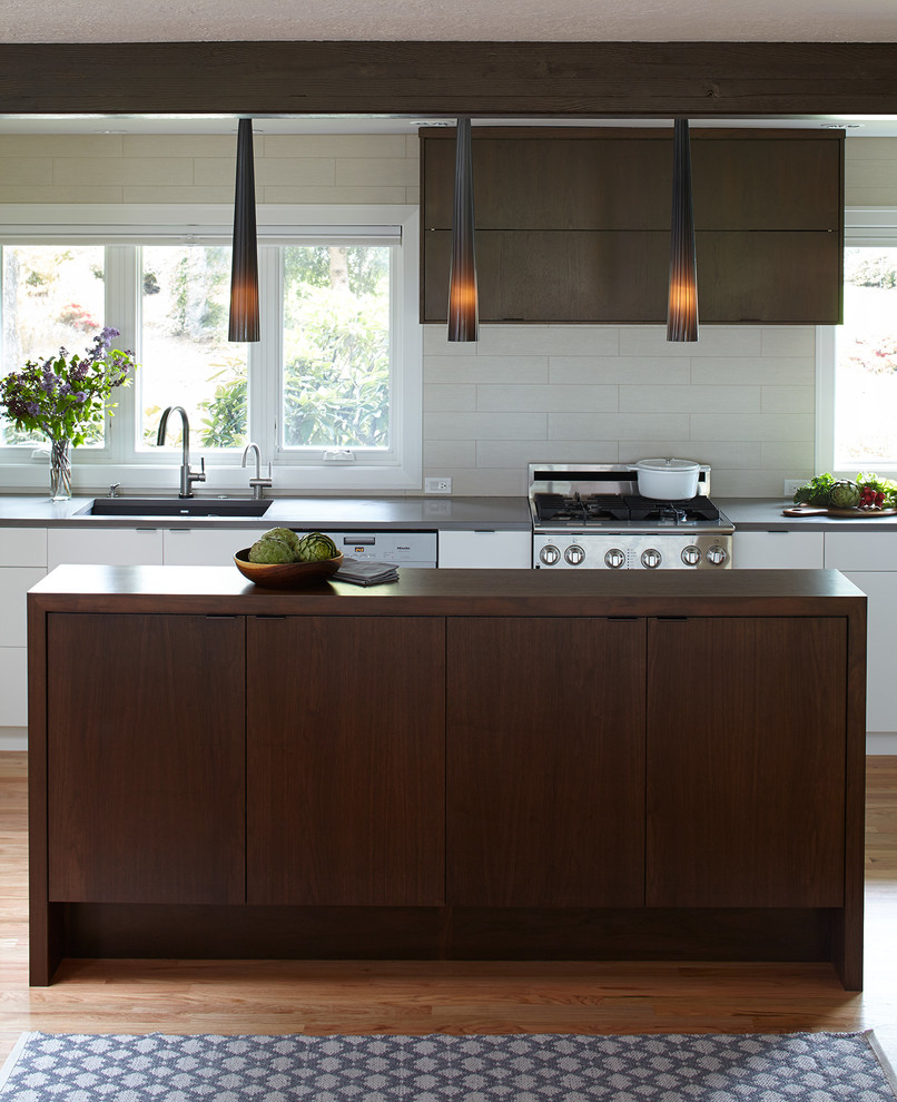 Photo of a large midcentury l-shaped eat-in kitchen in Portland with an undermount sink, flat-panel cabinets, dark wood cabinets, quartzite benchtops, white splashback, porcelain splashback, stainless steel appliances, light hardwood floors and with island.