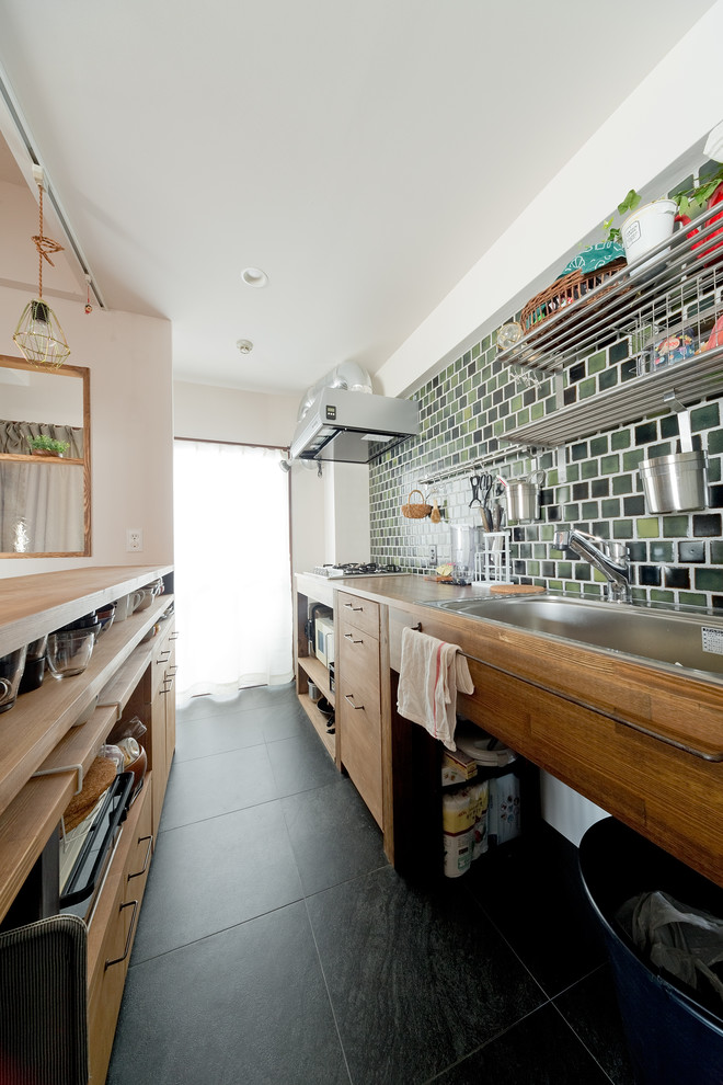 Photo of an asian single-wall open plan kitchen in Osaka with vinyl floors, black floor, beige benchtop, a single-bowl sink, flat-panel cabinets, medium wood cabinets, wood benchtops, green splashback and a peninsula.