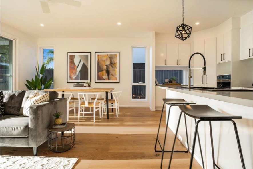 Design ideas for a small beach style eat-in kitchen in Gold Coast - Tweed with a double-bowl sink, flat-panel cabinets, white cabinets, solid surface benchtops, white splashback, stainless steel appliances, medium hardwood floors, with island, brown floor and beige benchtop.