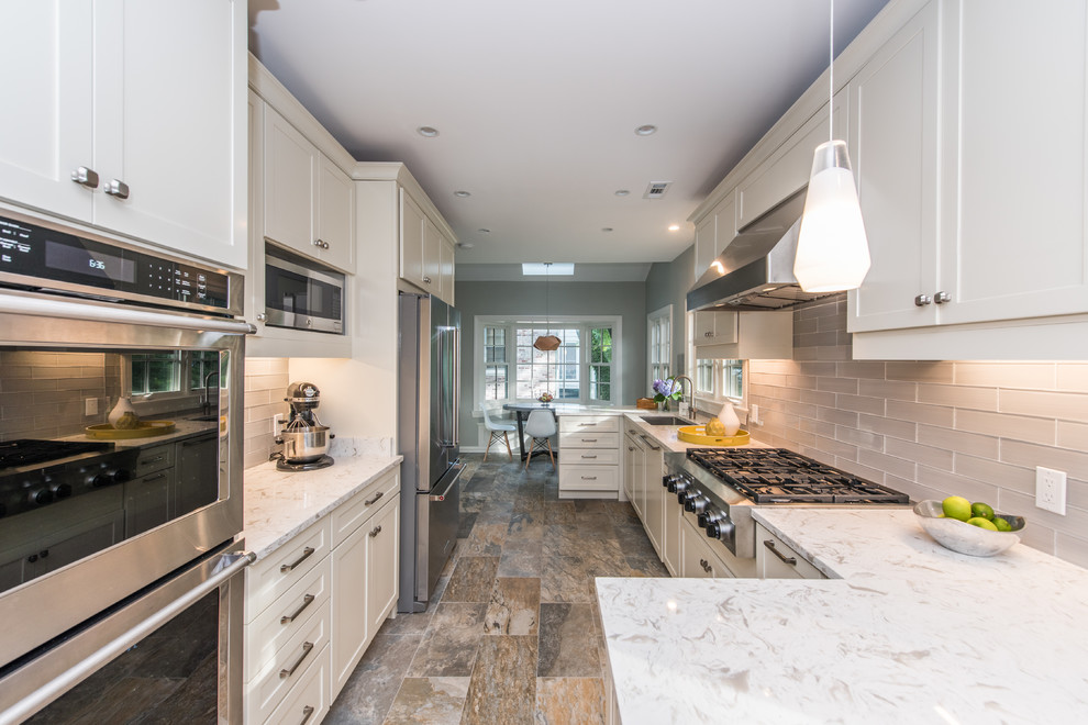 This is an example of a mid-sized transitional u-shaped kitchen in DC Metro with an undermount sink, shaker cabinets, white cabinets, solid surface benchtops, grey splashback, glass tile splashback, stainless steel appliances, porcelain floors, no island, multi-coloured floor and white benchtop.
