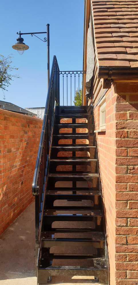 Inspiration for a mid-sized traditional metal straight staircase in Berkshire with open risers, metal railing and brick walls.