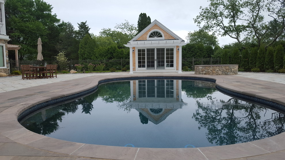 Mid-sized traditional backyard kidney-shaped pool in New York with natural stone pavers.