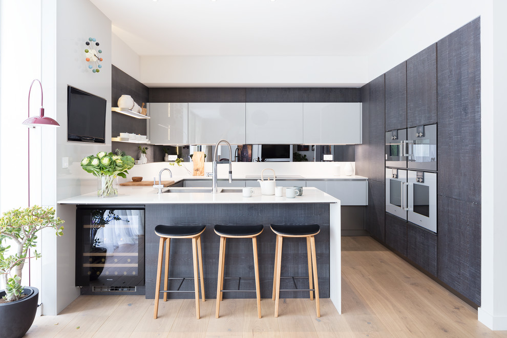Photo of a small contemporary u-shaped kitchen in London with a double-bowl sink, flat-panel cabinets, white cabinets, white appliances, light hardwood floors and a peninsula.