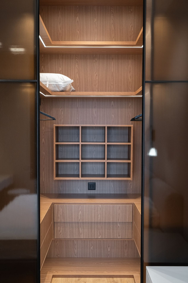 This is an example of a medium sized contemporary gender neutral walk-in wardrobe in Moscow with flat-panel cabinets, medium wood cabinets and medium hardwood flooring.