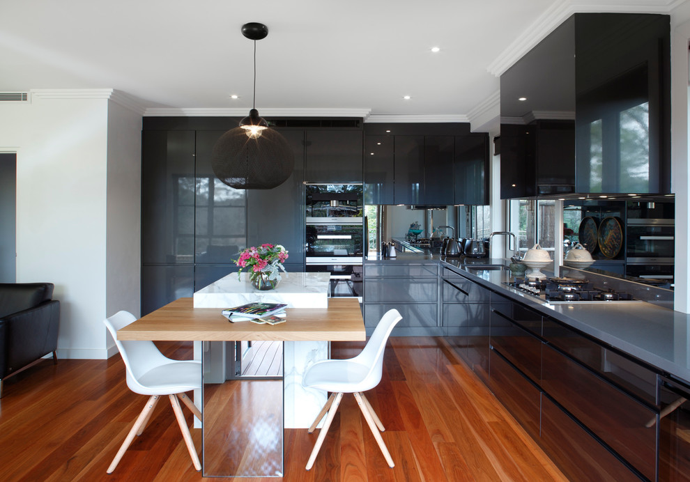 This is an example of a mid-sized contemporary l-shaped eat-in kitchen in Sydney with an undermount sink, recessed-panel cabinets, grey cabinets, marble benchtops, metallic splashback, mirror splashback, black appliances, light hardwood floors and with island.