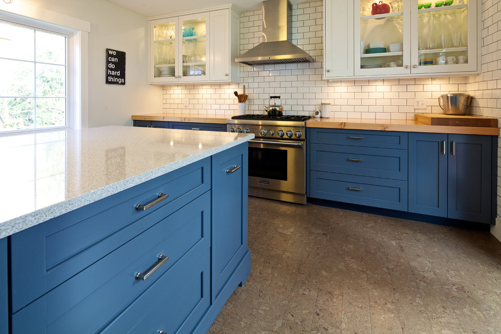 Photo of a mid-sized country l-shaped open plan kitchen in Vancouver with a farmhouse sink, shaker cabinets, blue cabinets, quartzite benchtops, white splashback, subway tile splashback, stainless steel appliances, cork floors and with island.