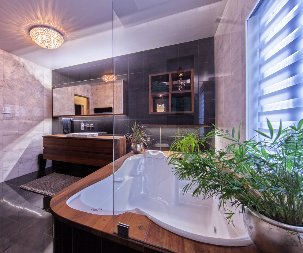 Mid-sized contemporary master bathroom in Montreal with a drop-in sink, flat-panel cabinets, medium wood cabinets, wood benchtops, an undermount tub, an open shower, a wall-mount toilet, black tile and stone tile.