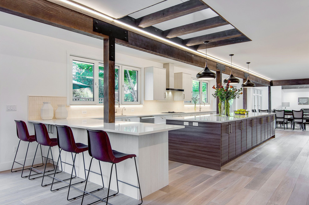 Photo of an expansive midcentury galley open plan kitchen in Portland with an undermount sink, flat-panel cabinets, white cabinets, quartz benchtops, white splashback, limestone splashback, stainless steel appliances, light hardwood floors, with island, brown floor and white benchtop.