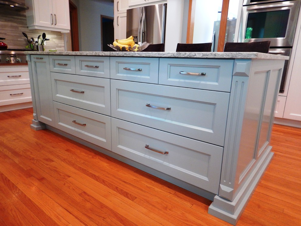 Example of a large transitional l-shaped light wood floor eat-in kitchen design with an undermount sink, recessed-panel cabinets, white cabinets, quartz countertops, gray backsplash, stone tile backsplash, stainless steel appliances and an island