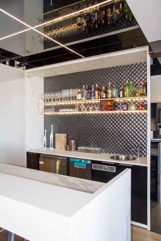 Photo of a large modern galley seated home bar in Melbourne with flat-panel cabinets, a drop-in sink, black cabinets, tile benchtops, grey splashback, mosaic tile splashback, medium hardwood floors, brown floor and white benchtop.