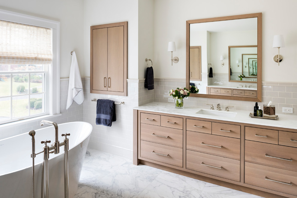 This is an example of a mid-sized transitional master bathroom in New York with beaded inset cabinets, light wood cabinets, a freestanding tub, a corner shower, a two-piece toilet, gray tile, ceramic tile, white walls, marble floors, an undermount sink and marble benchtops.