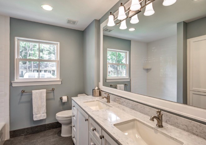 Photo of a mid-sized transitional master bathroom in Houston with recessed-panel cabinets, white cabinets, an alcove tub, a shower/bathtub combo, a two-piece toilet, white tile, ceramic tile, blue walls, porcelain floors, an undermount sink, engineered quartz benchtops and grey floor.