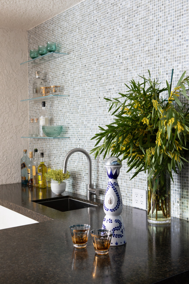 This is an example of a mid-sized modern l-shaped wet bar in Los Angeles with an undermount sink, granite benchtops, blue splashback, mosaic tile splashback, concrete floors, beige floor and black benchtop.