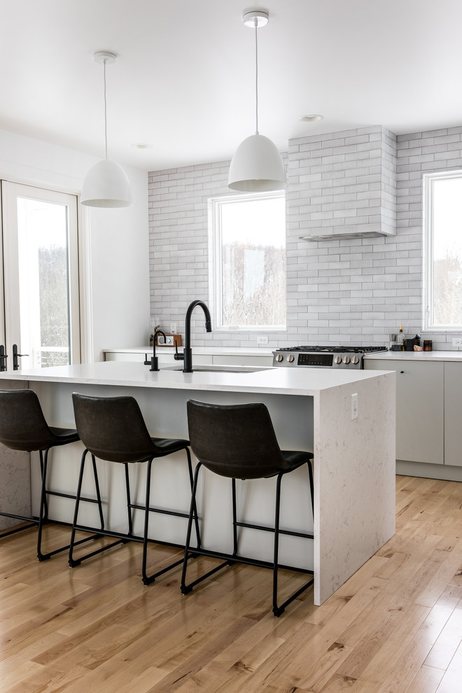 Design ideas for a large scandinavian single-wall eat-in kitchen in Grand Rapids with an undermount sink, flat-panel cabinets, grey cabinets, quartzite benchtops, grey splashback, brick splashback, stainless steel appliances, light hardwood floors, with island, beige floor and white benchtop.