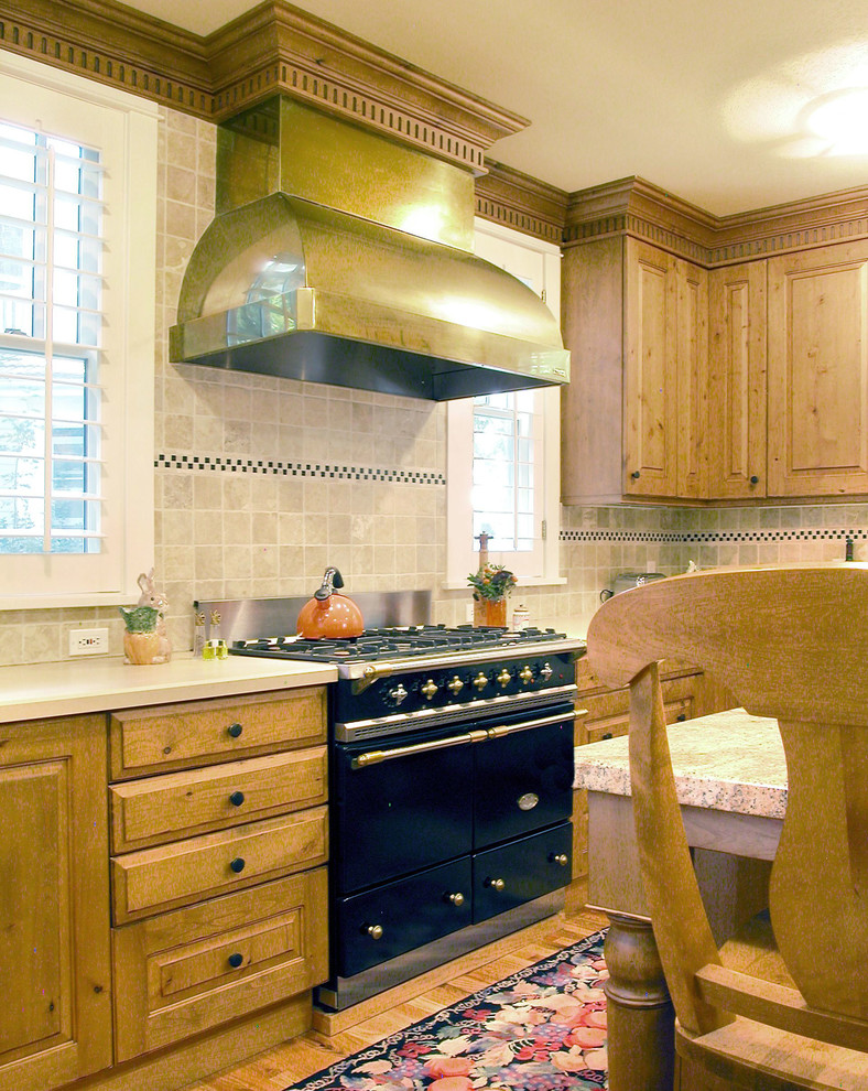Example of a mid-sized arts and crafts l-shaped medium tone wood floor enclosed kitchen design in Denver with a farmhouse sink, raised-panel cabinets, medium tone wood cabinets, granite countertops, beige backsplash, stone tile backsplash, black appliances and beige walls