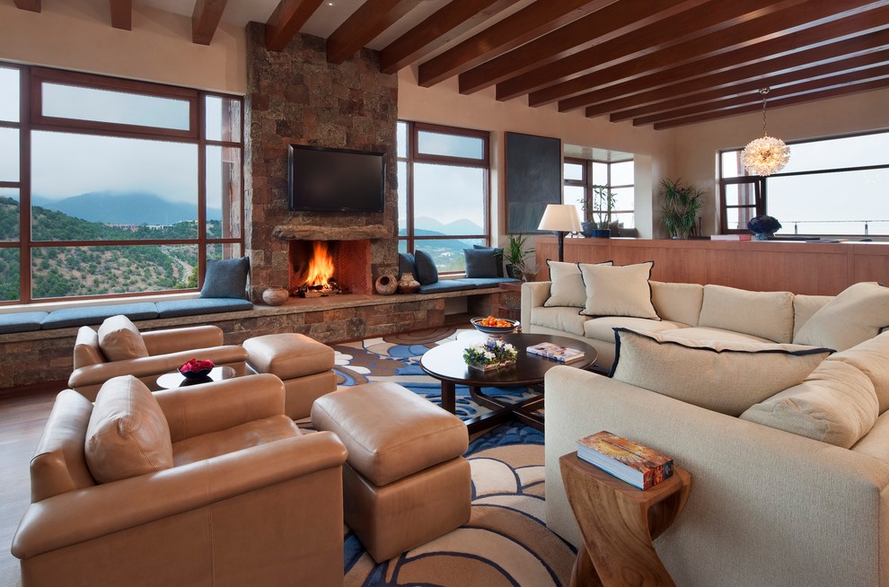 This is an example of a large open concept family room in Albuquerque with beige walls, medium hardwood floors, a standard fireplace, a stone fireplace surround, a wall-mounted tv and brown floor.